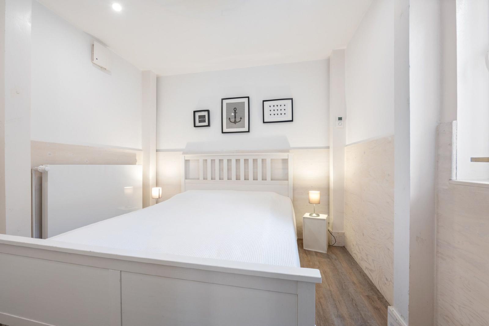 Schlafzimmer mit weißem Bett, zwei Nachttischen und Wandbildern.