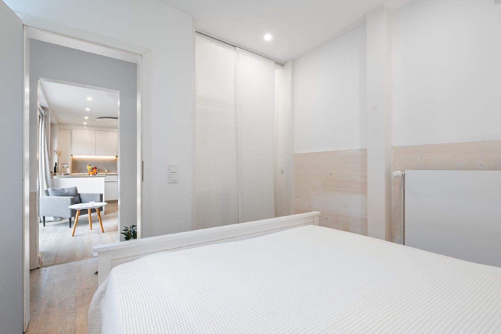 Schlafzimmer mit Bett und Blick in Wohnbereich mit Küchenzeile.