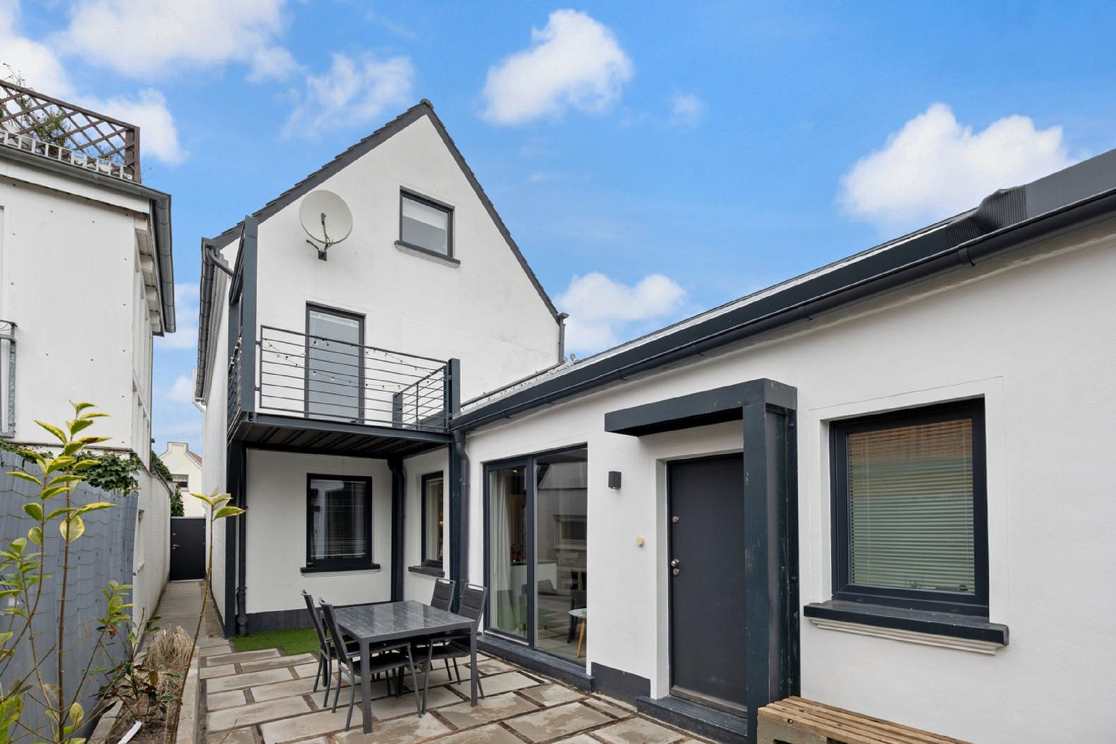 Wohnhaus mit Terrasse, Tisch und Stühlen. Schwarze Fensterrahmen und Tür. Weiße Fassade.
