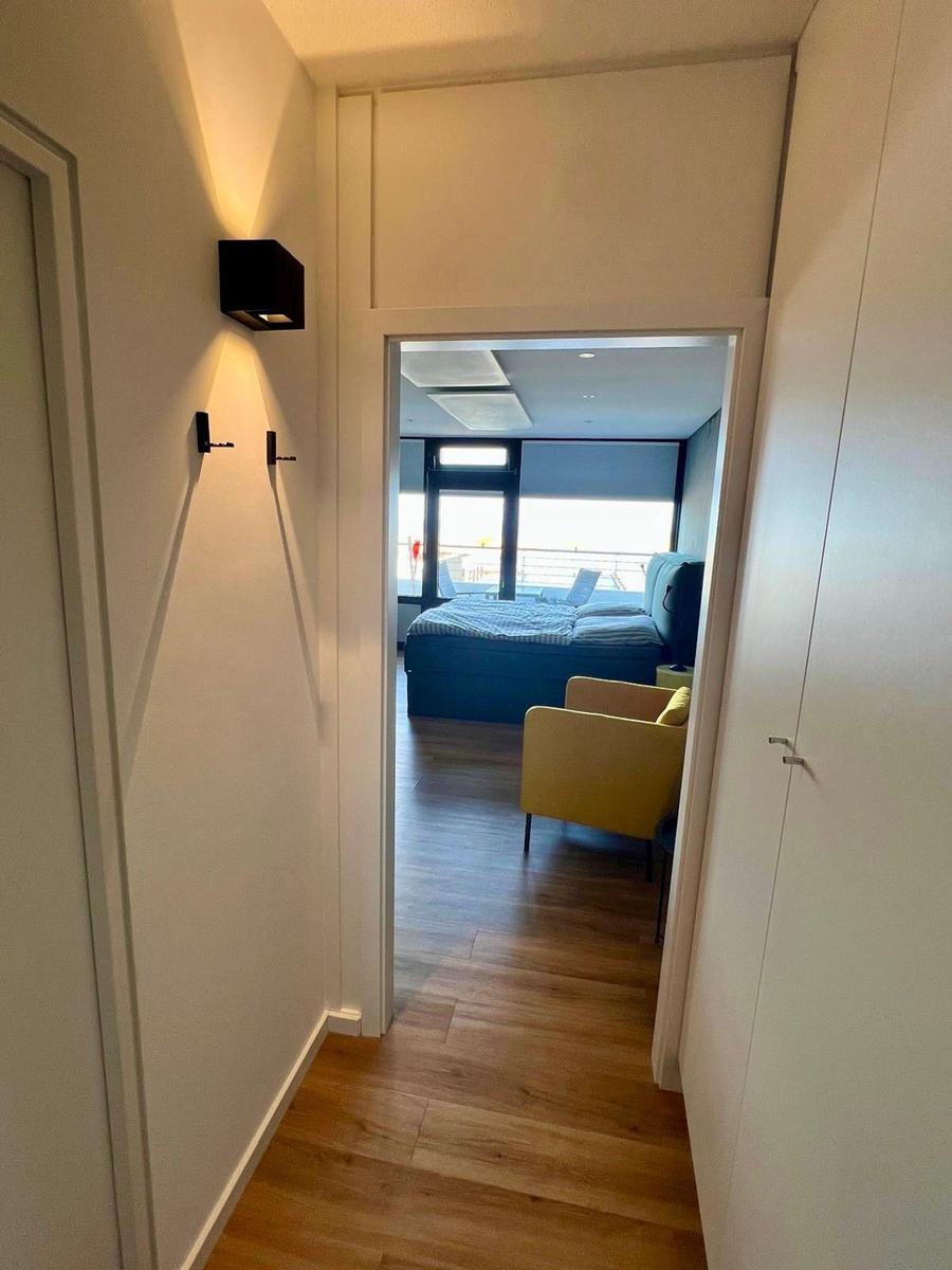 Flur mit Holzboden führt in ein Schlafzimmer mit Bett und Sessel.