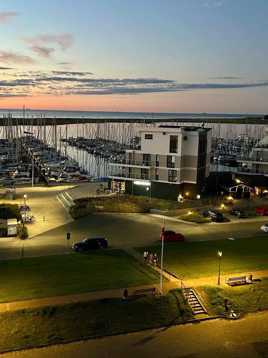 Marina mit Booten und modernem Gebäude bei Sonnenuntergang.