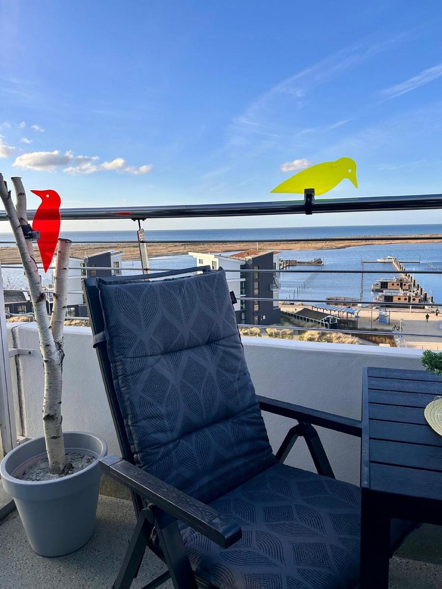 Terrasse mit Sessel, Tisch und Blick auf Meer und Hafen.