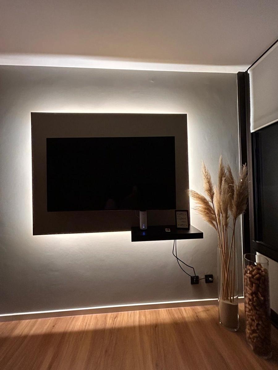TV an der Wand mit eingebauter Beleuchtung und dekorativen Pflanzen im Vordergrund.