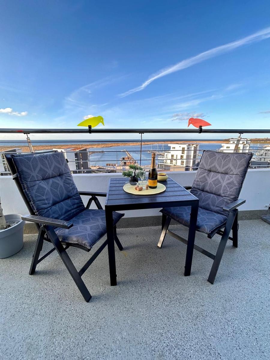 Terrasse mit Tisch, zwei Stühlen und Meerblick. Auf dem Tisch steht eine Flasche Champagner.