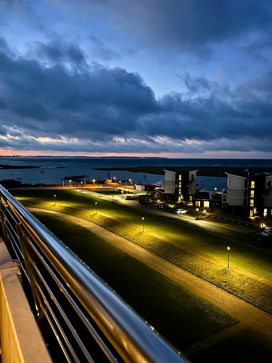 Abendansicht vom Balkon mit Blick auf beleuchtete Grünfläche und Meeresufer.