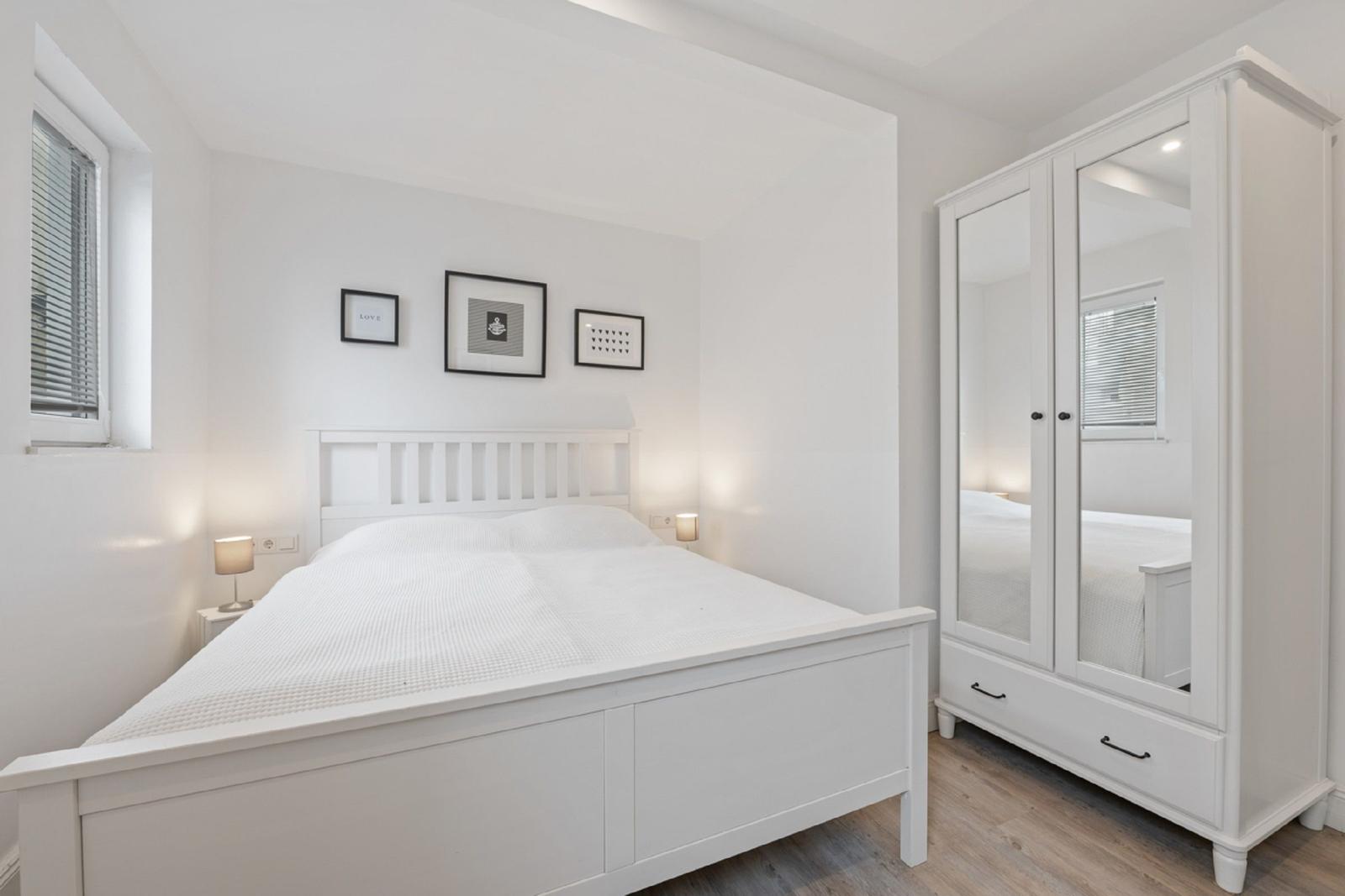 Schlafzimmer mit weißem Bett, Kleiderschrank und Fenster.