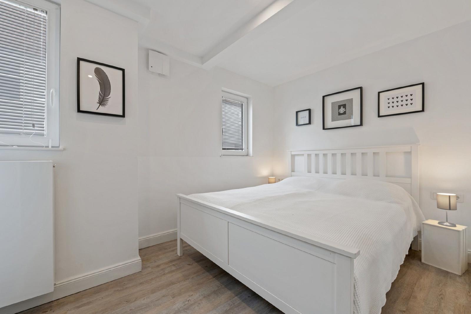 Ein Schlafzimmer mit weißem Bett, Holzboden und Wandbildern.