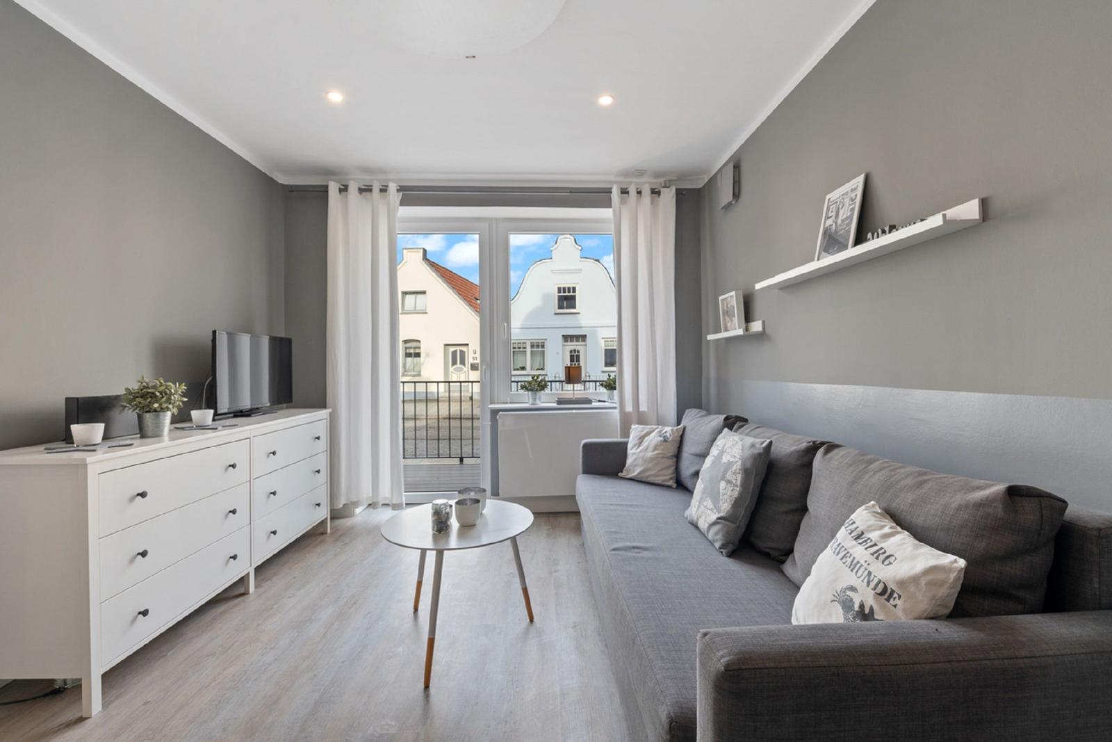 Wohnzimmer mit Sofa, Couchtisch und Fernseher. Balkon mit Blick auf Gebäude.