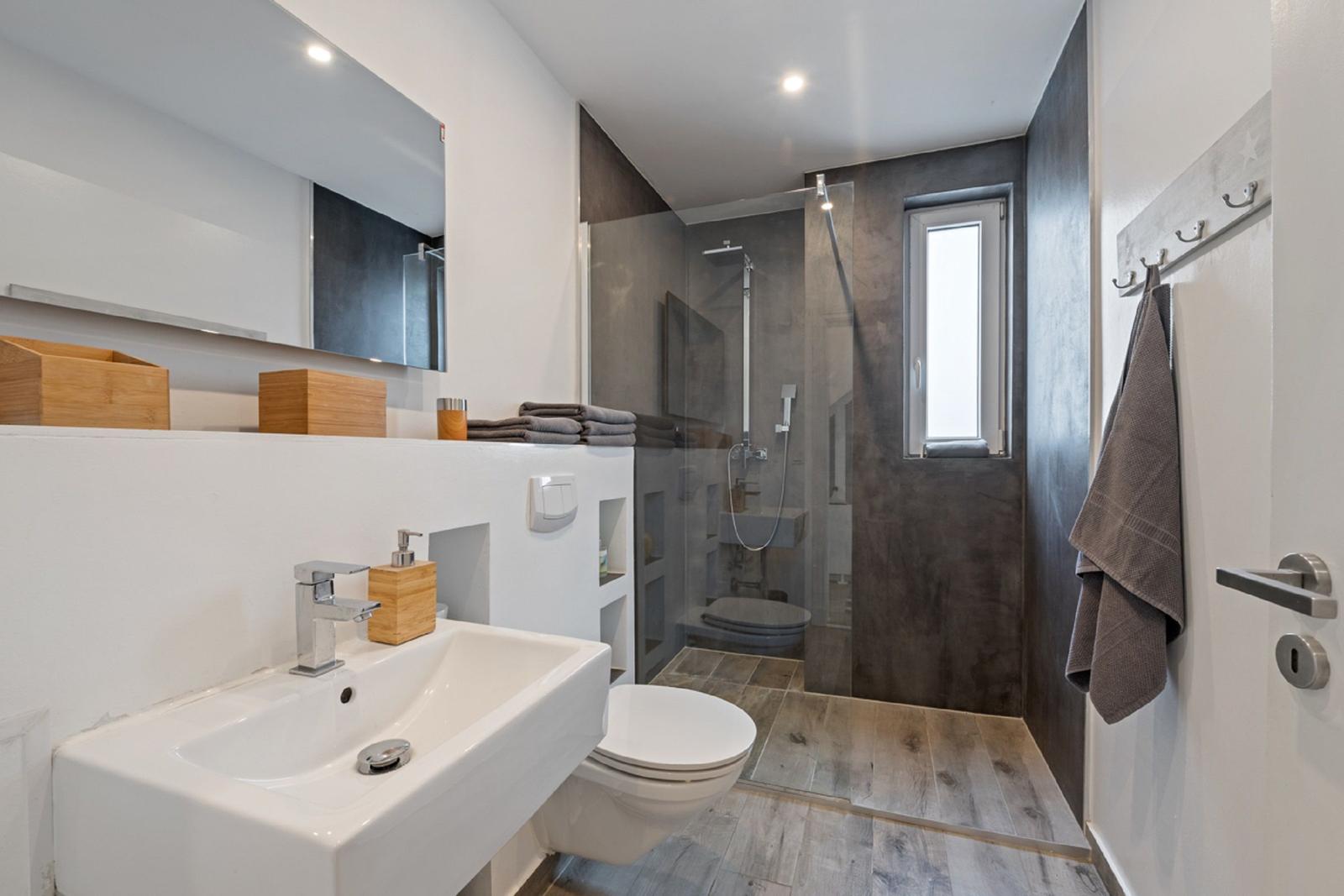 Badezimmer mit Dusche, Waschbecken und Toilette. Holzoptik und dunkle Wandfarbe.