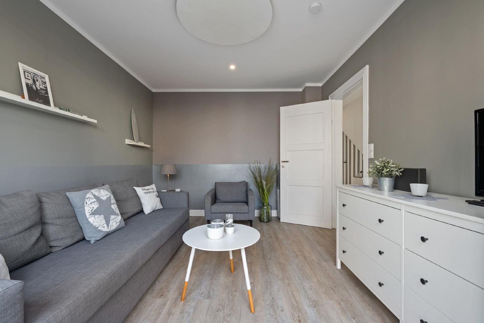 Wohnzimmer mit grauem Sofa, weißem Tisch und Schrank. Holzfußboden und Wanddekoration.