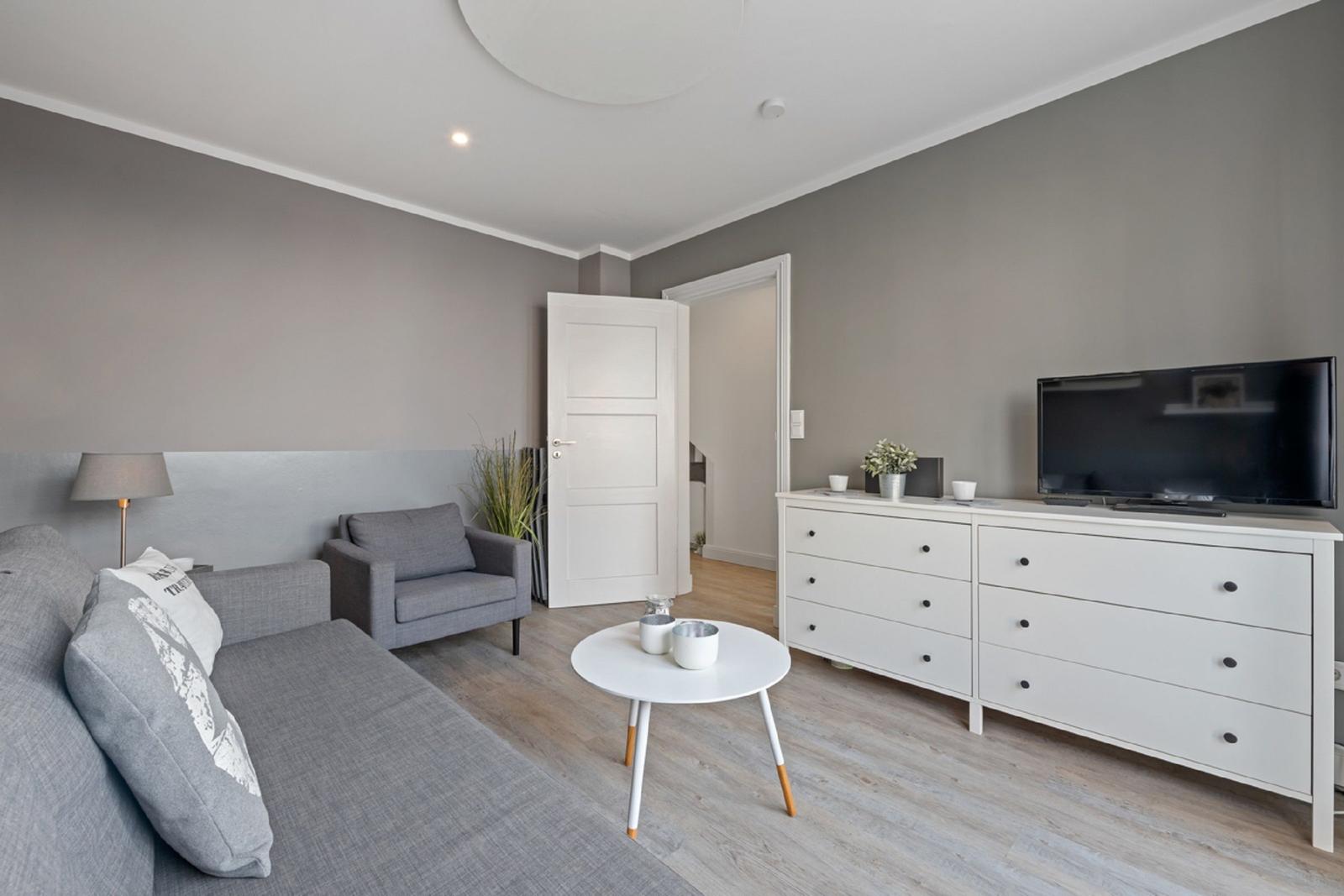 Wohnzimmer mit Sofa, Sessel, Couchtisch und TV-Schrank.