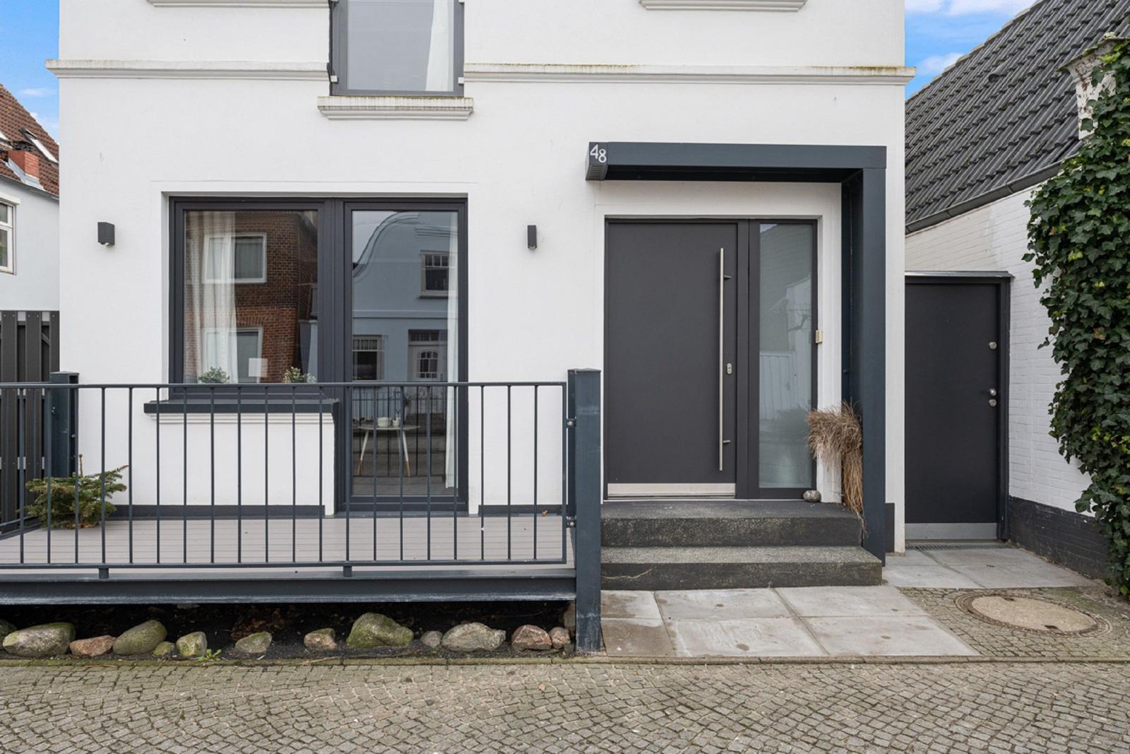 Moderne weiße Fassade mit dunkler Tür und Balkon. Hausnummer 48.