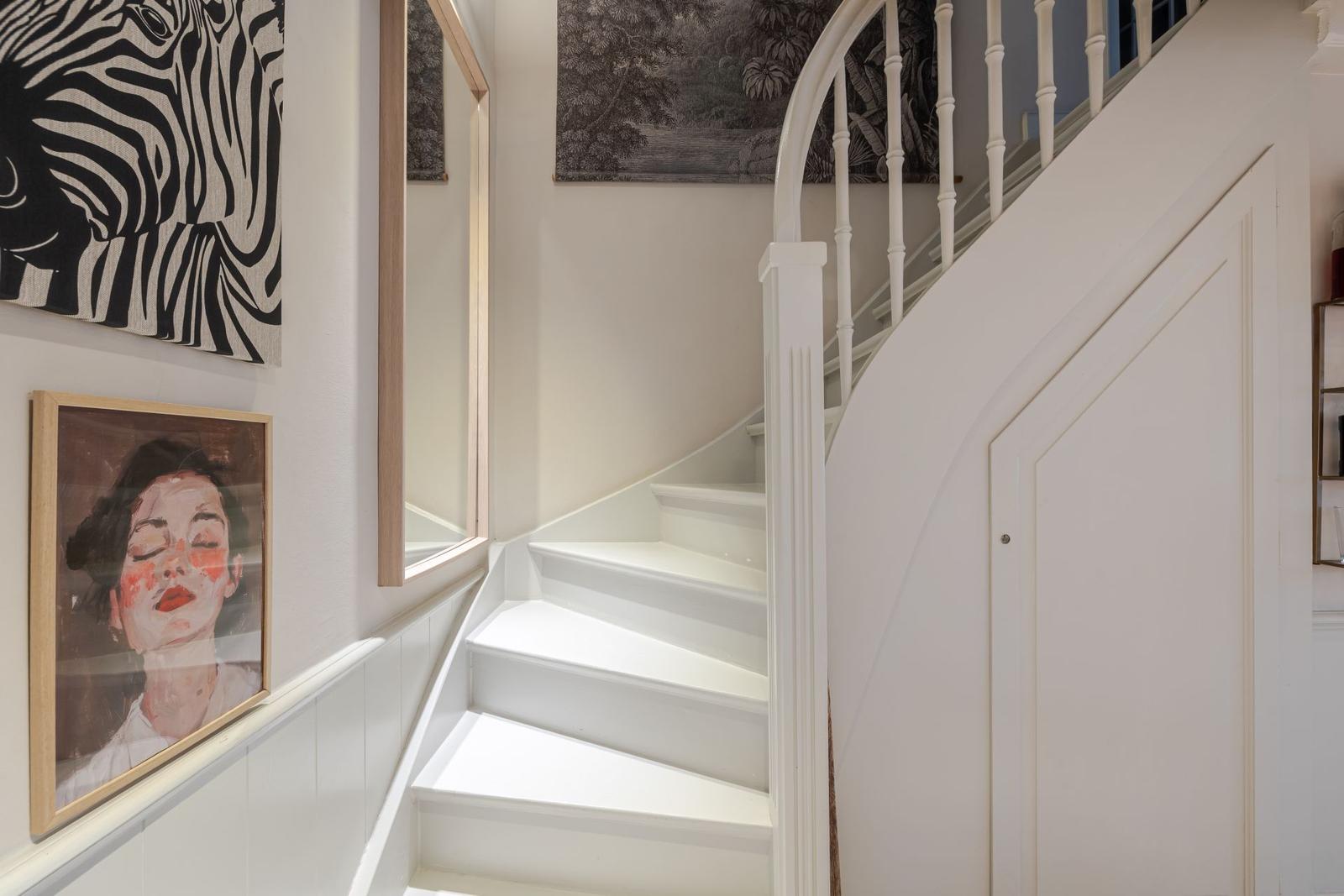 Weiße Treppe mit geschwungenem Geländer und Wandbildern an den Wänden.