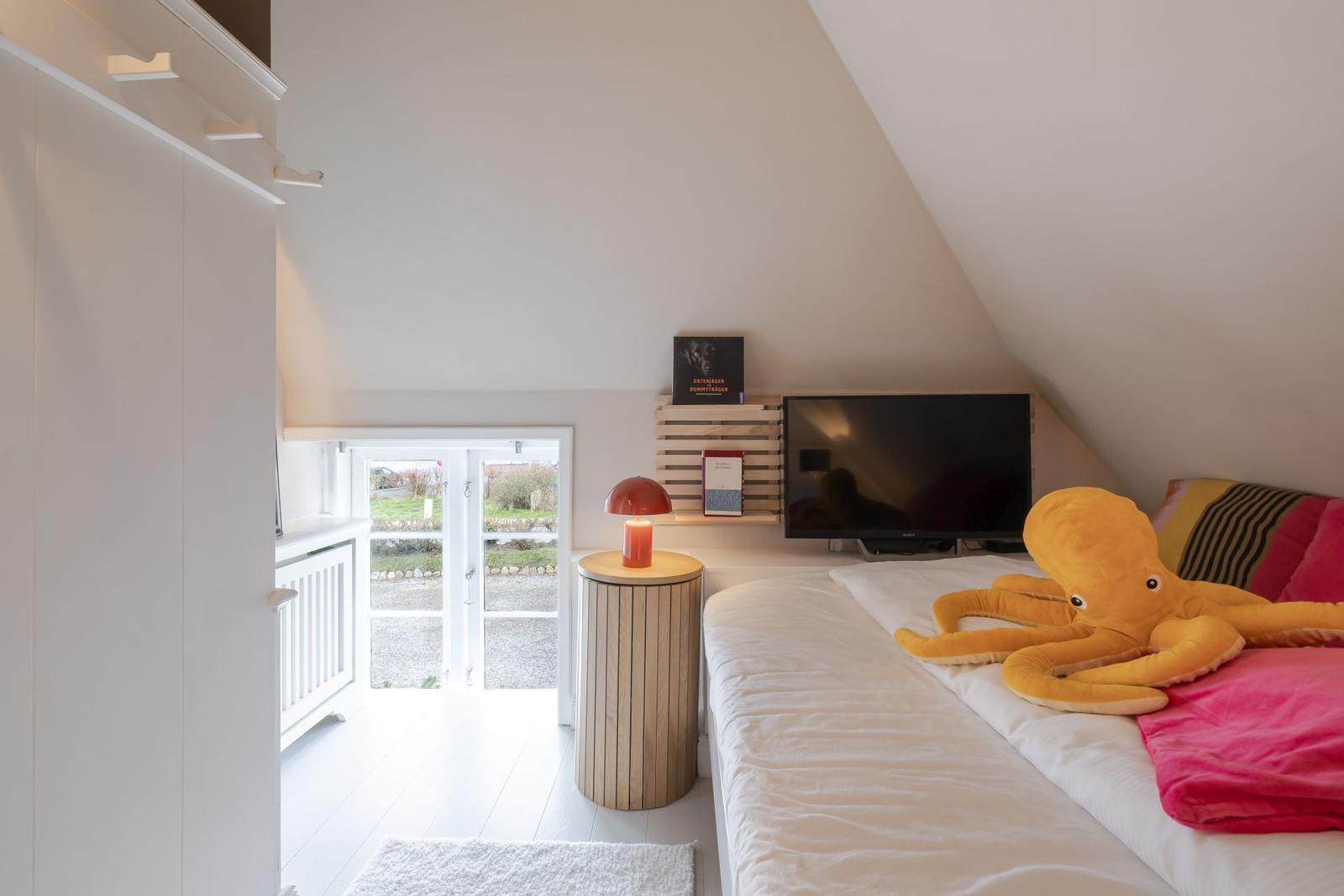 Schlafzimmer mit Dachschräge, Bett, Fernseher und Fenster zur Außenterrasse.