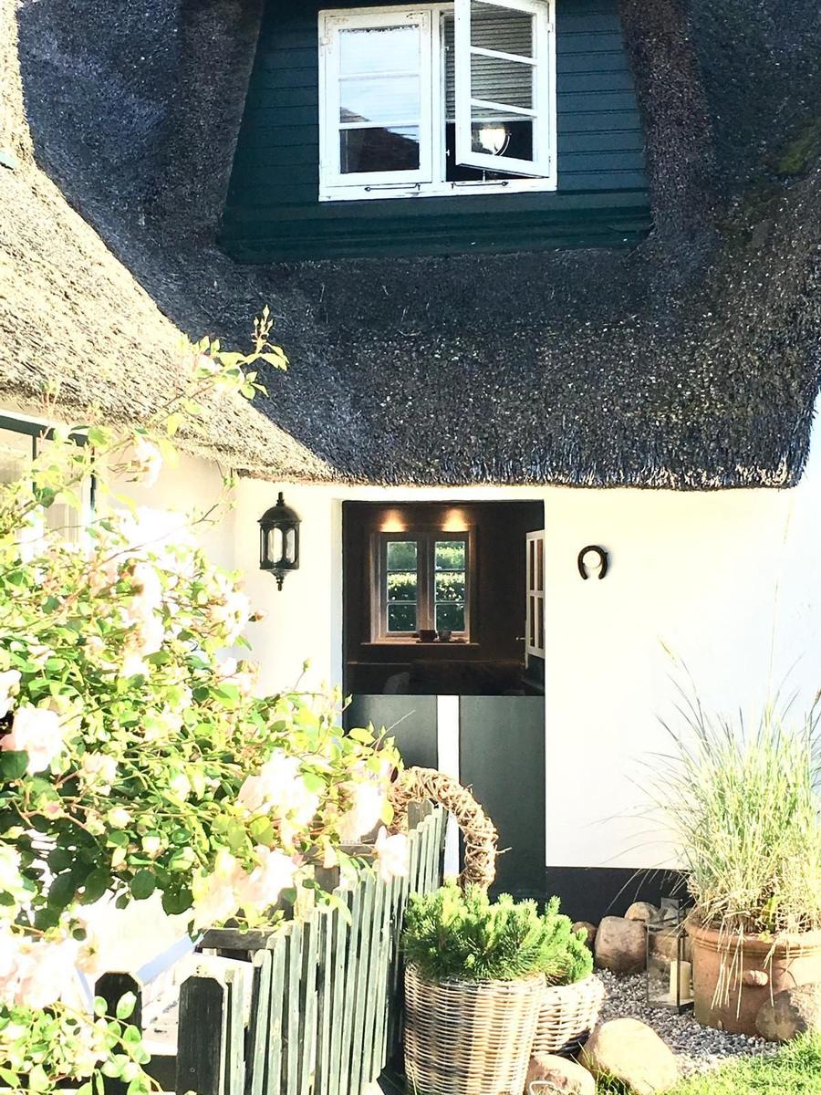 Haus mit Strohdach, weißer Fassade und Garten mit Pflanzen.