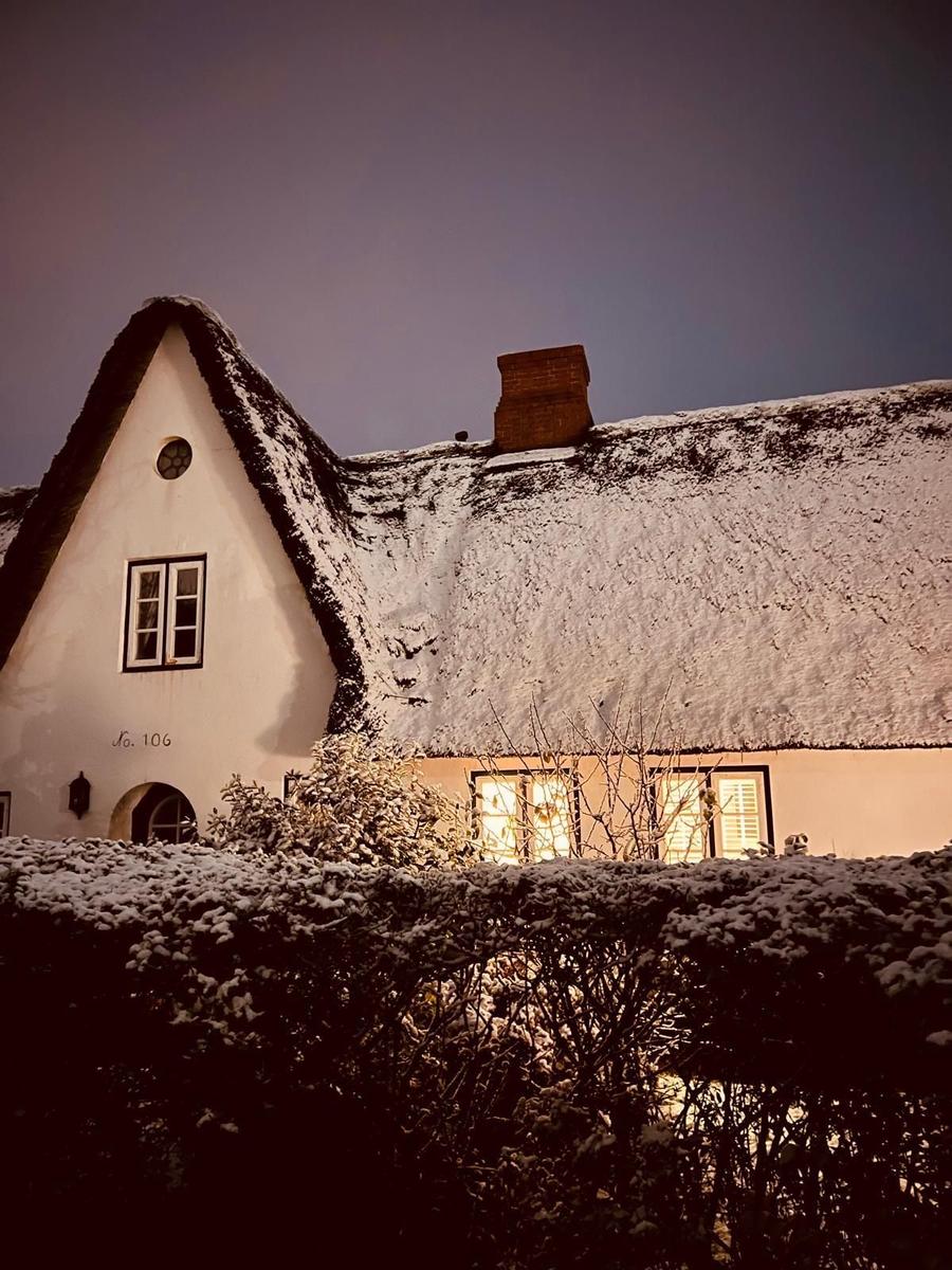 Schneebedecktes Haus mit strohgedecktem Dach und beleuchteten Fenstern.