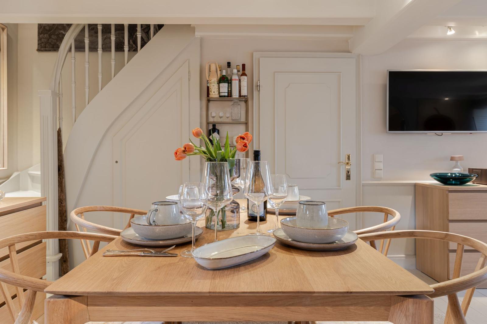 Esszimmer mit Tisch, Stühlen und Blumen. Hintergrund: Treppe und Fernseher.