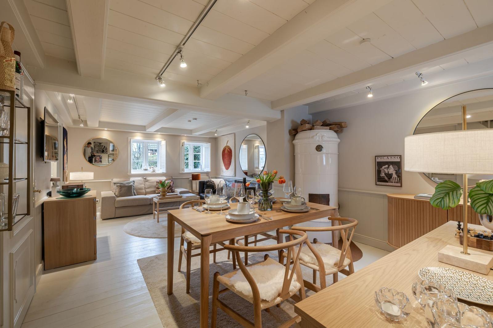 Esszimmer mit Holztisch und Stühlen, Wohnbereich mit Sofa und Fenstern, weiße Decke mit Balken.