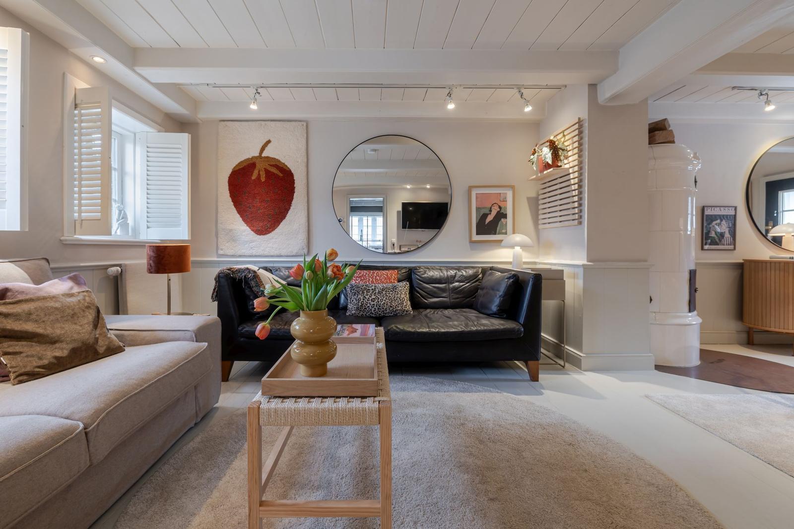 Wohnzimmer mit Ledersofa, runden Spiegel und Wandbild einer Erdbeere.