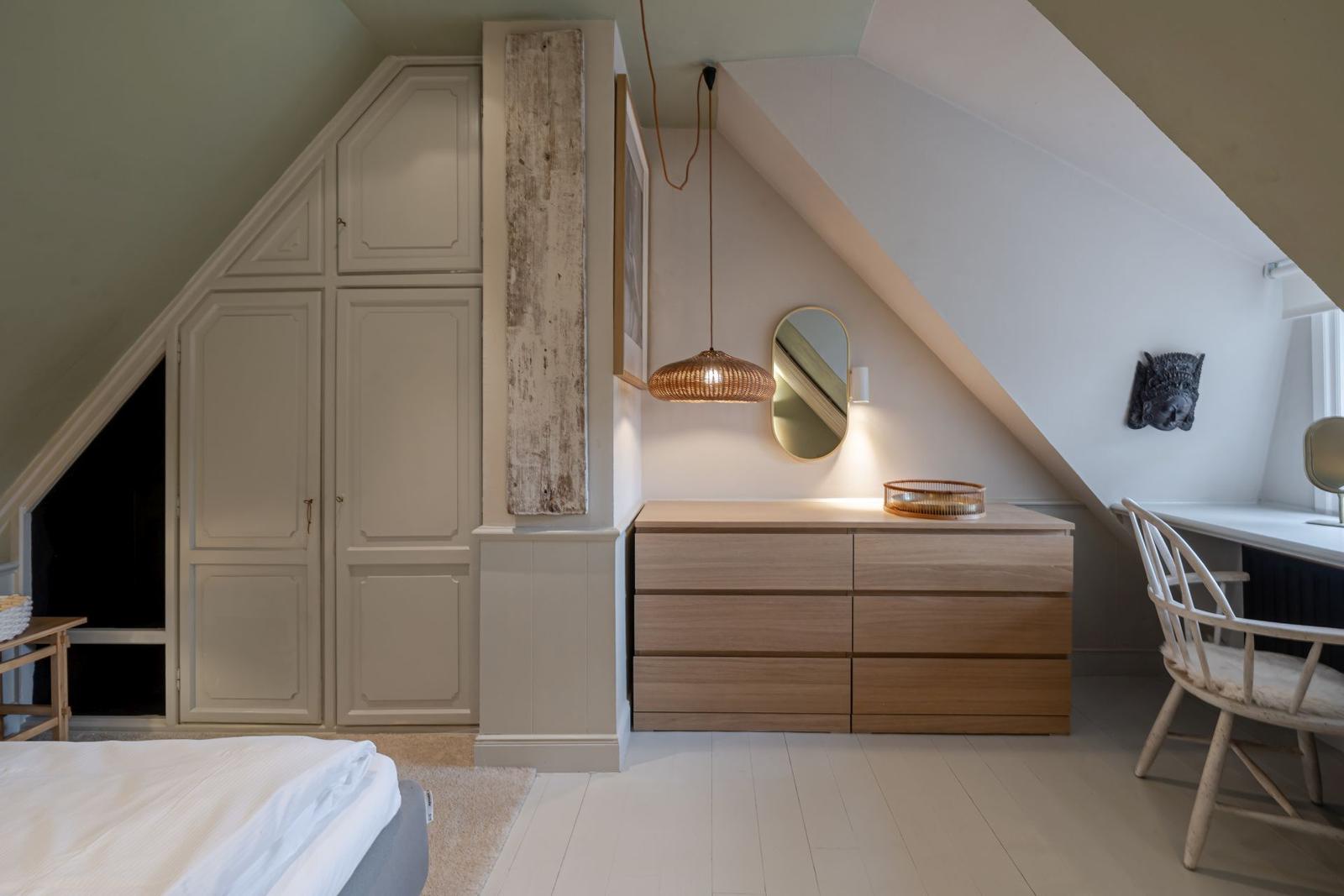 Schlafzimmer mit Kleiderschrank, Schreibtisch und Holzkommode unter Dachschrägen.