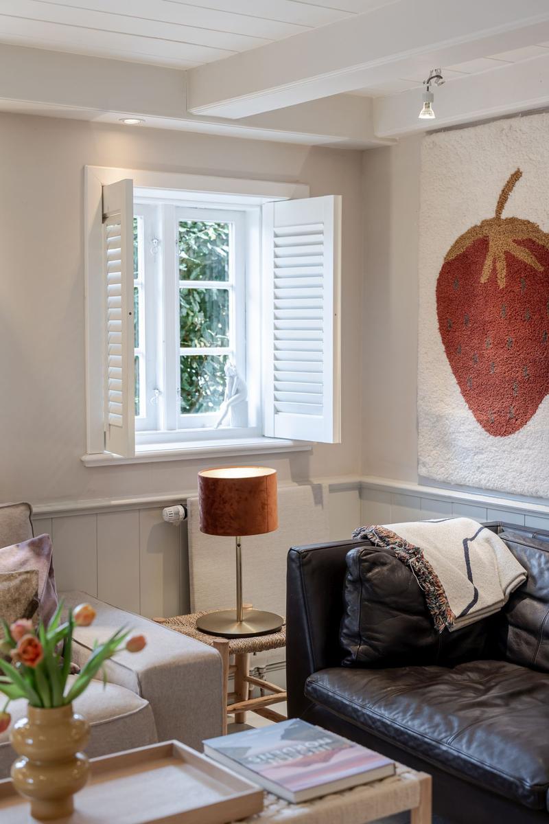 Ein Wohnzimmer mit Fenster, Schiebetüren, Ledersofa und Wandbild mit Erdbeere.