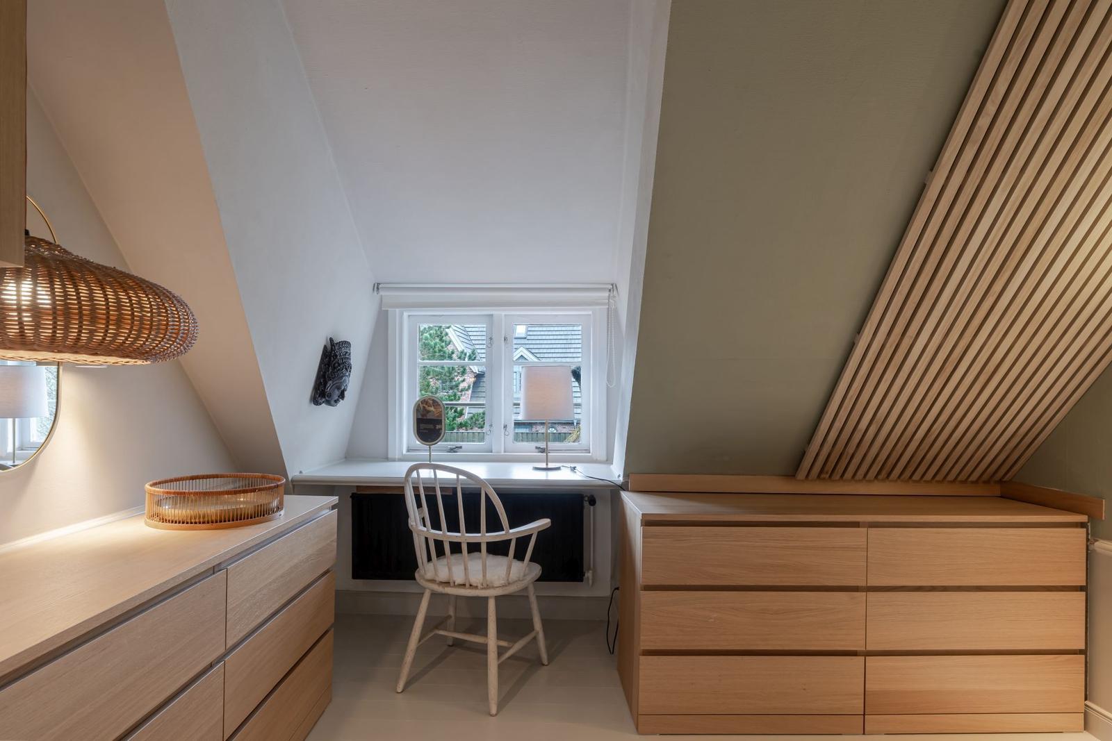Schlafzimmer mit Schreibtisch, Stuhl und Holzschränken unter Dachschrägen.