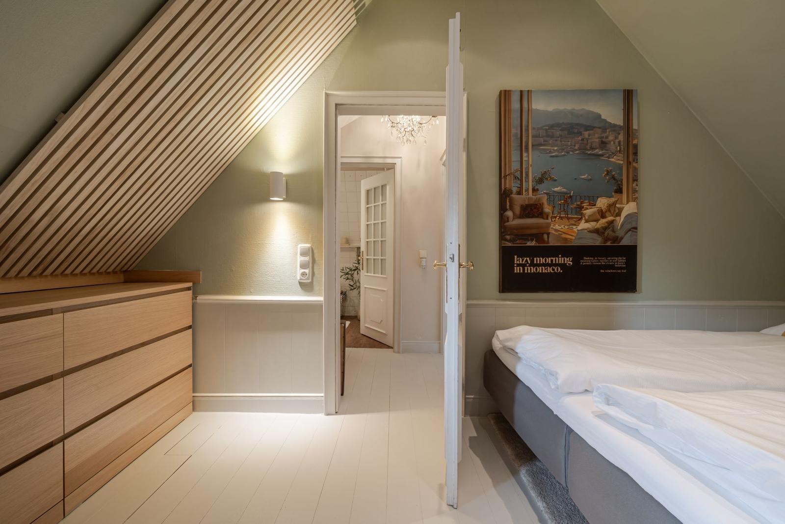 Schlafzimmer mit Dachschrägen, Bett und Kleiderschrank. Tür führt in Bad.