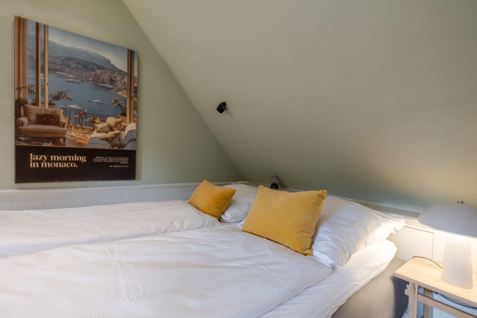 Schlafzimmer mit Dachschräge, Bett mit gelben Kissen und Wandbild.