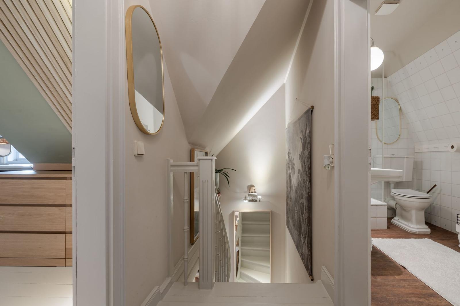 Treppenhaus mit Spiegel und Gemälde, Blick in Bad mit Toilette und Waschbecken.
