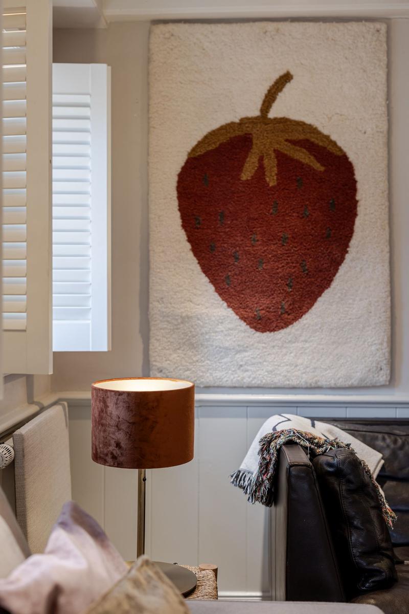 Wohnzimmer mit Strickteppich in Form einer Erdbeere, Lampe und Ledersofa.
