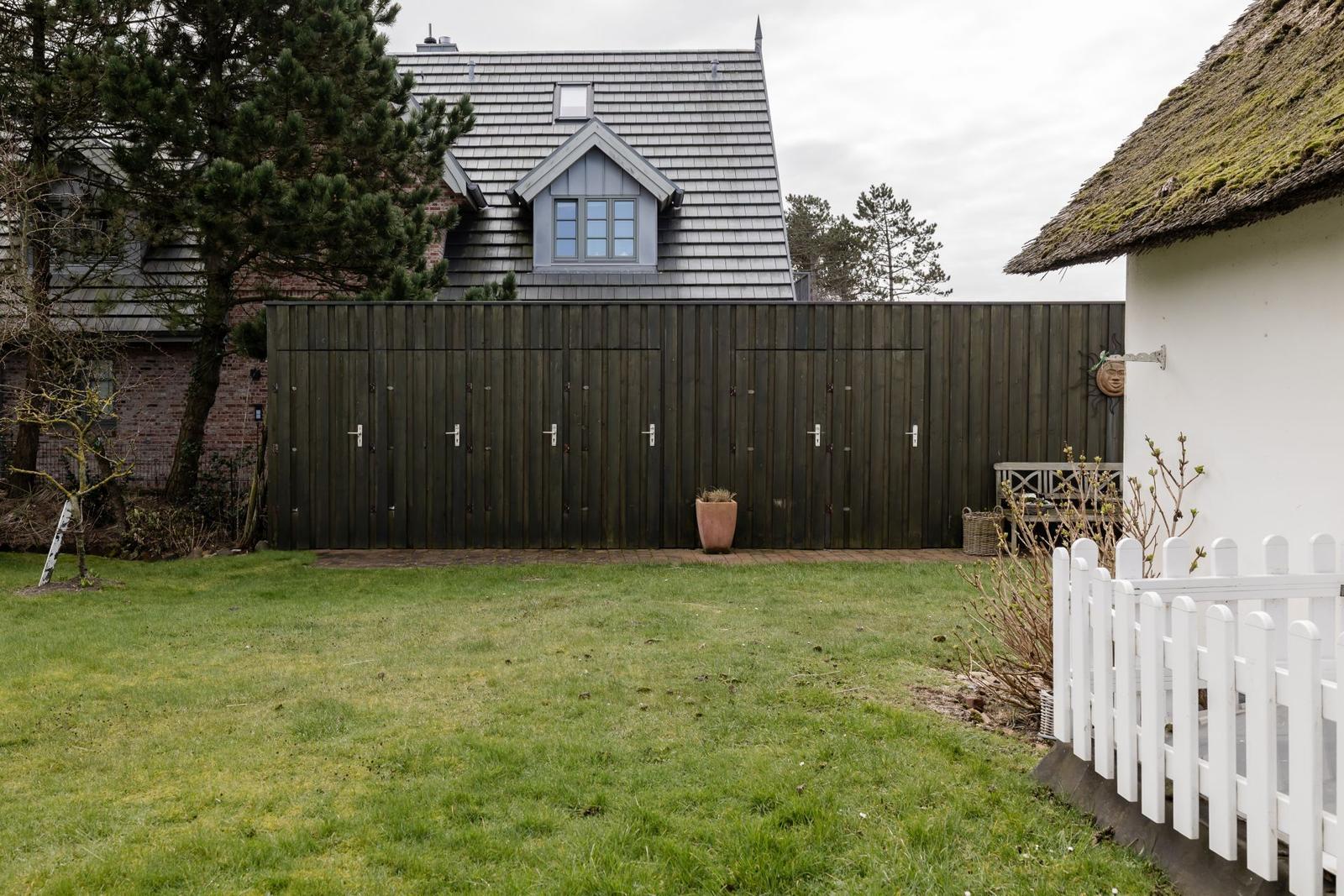 Hinterhof mit Grünfläche, Holz-Zaun und Gartenhaus mit Schilfdecke.