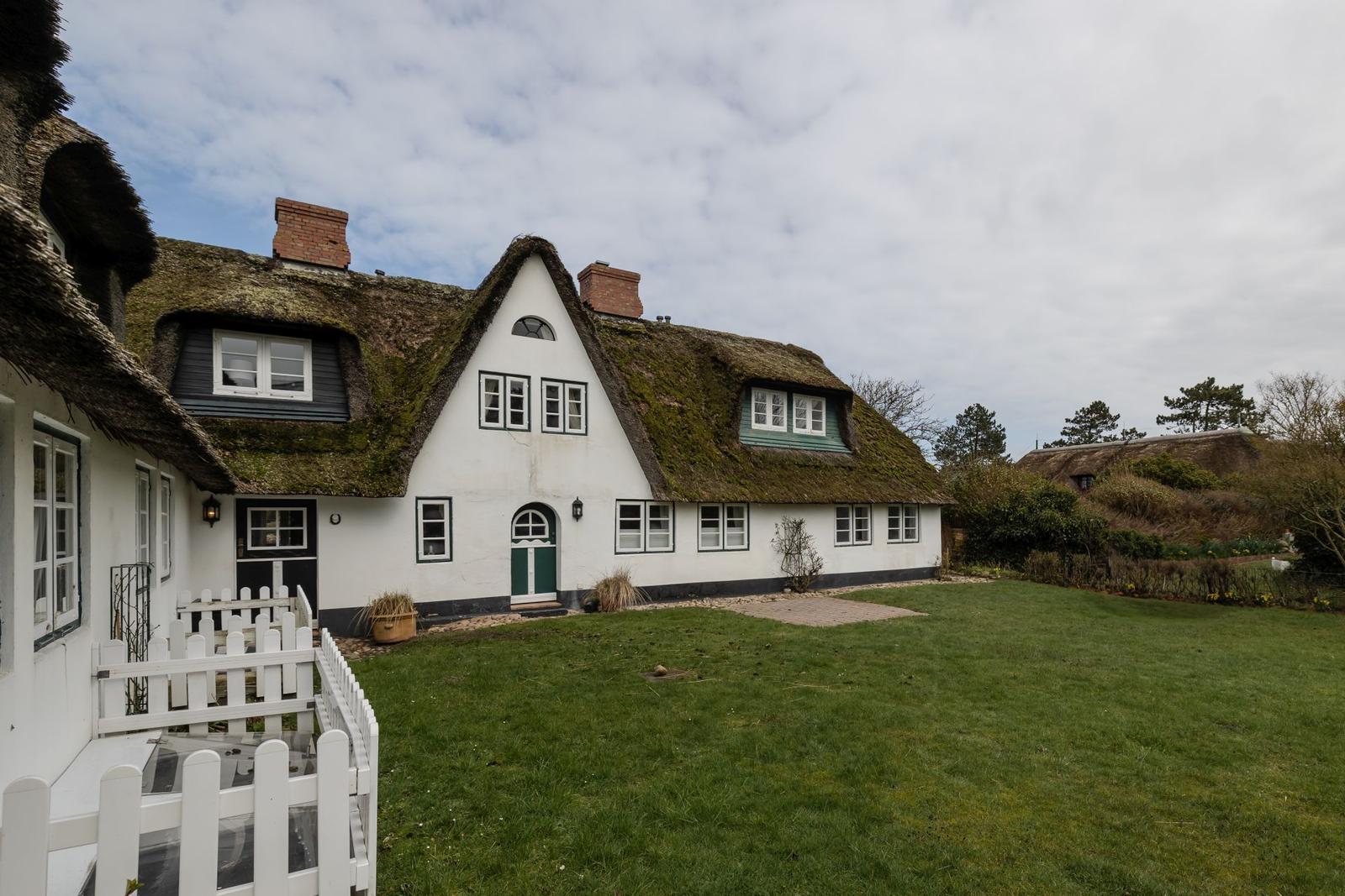 Traditionelles Haus mit Strohdach und weißer Fassade im Garten