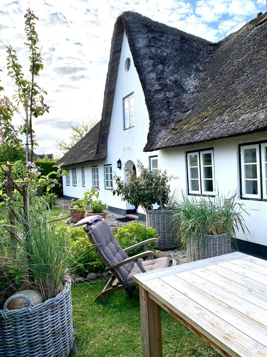 Haus mit strohgedecktem Dach und Gartenbereich mit Holztisch und Liegestuhl.