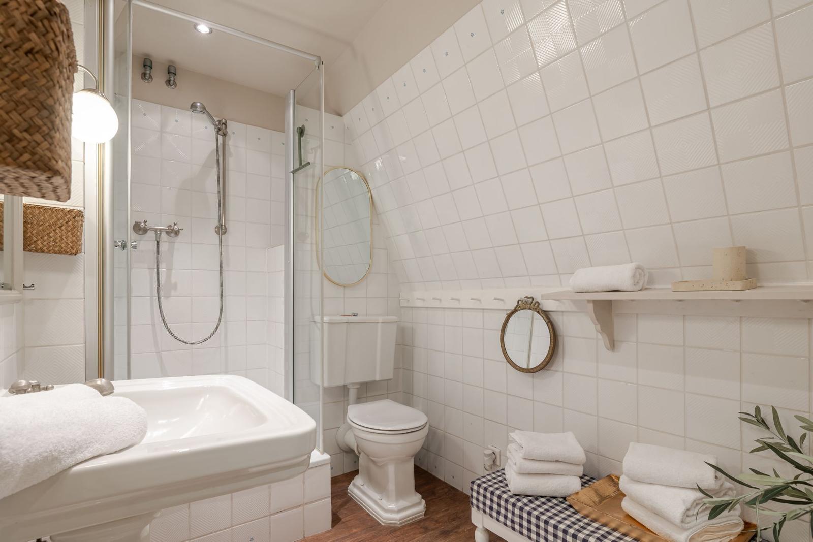 Badezimmer mit Dusche, Waschbecken und Toilette. Weiße Fliesen und Holzboden.