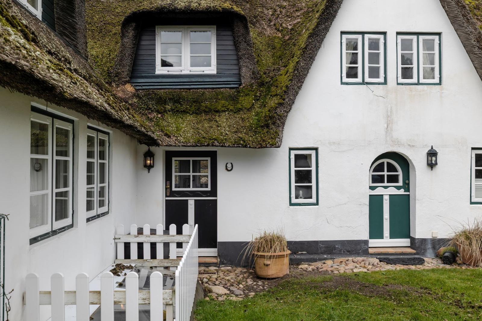 Haus mit grünem Dach und weißen Wänden, zwei Eingänge und Fenster mit grünen Rahmen.