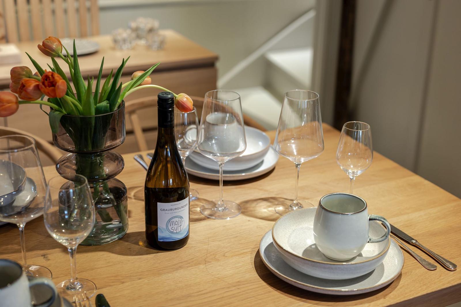 Gedeckter Tisch mit Weinflasche, Gläsern und Tulpen im Vase.