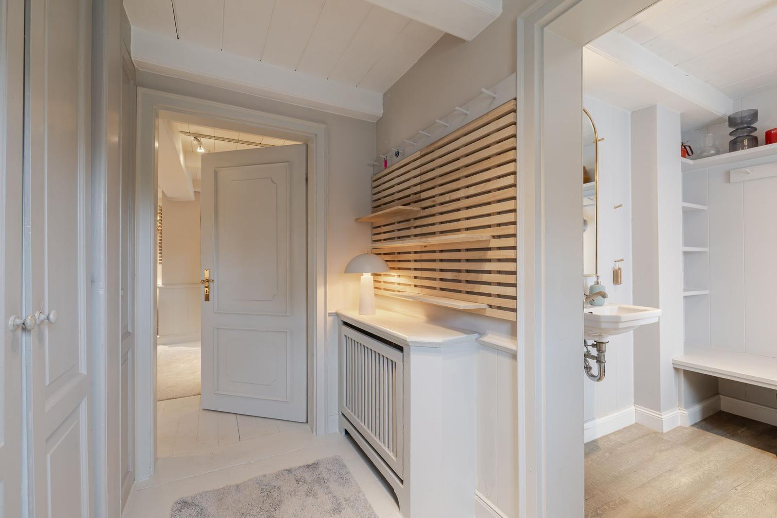 Flur mit Holzregal, Waschbecken und Tür zum Schlafzimmer.