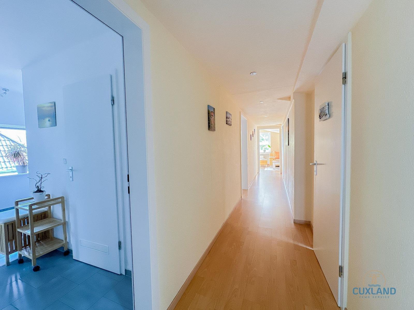 Flur mit Holzboden und Türen zu Räumen. An der Wand hängen Bilder.