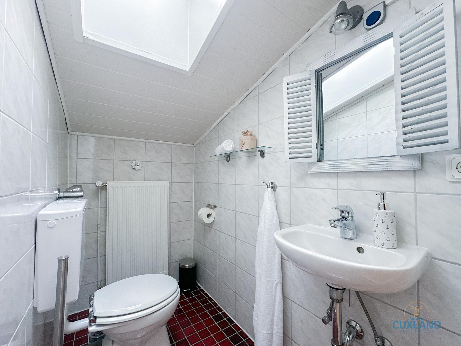 Badezimmer mit Toilette, Waschbecken und Spiegel. Rote Fliesenboden und weiße Wandfliesen.