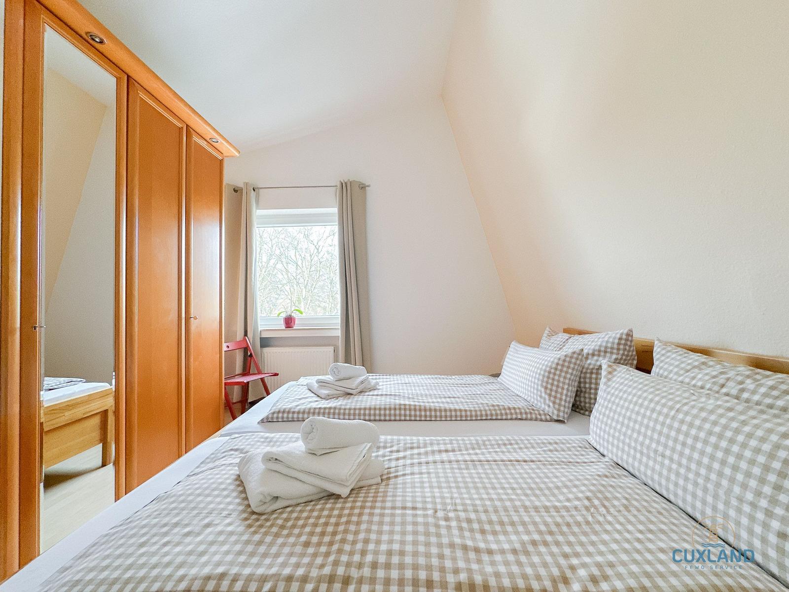 Zimmer mit Doppelbett, Kleiderschrank und Fenster mit Blick auf Bäume.