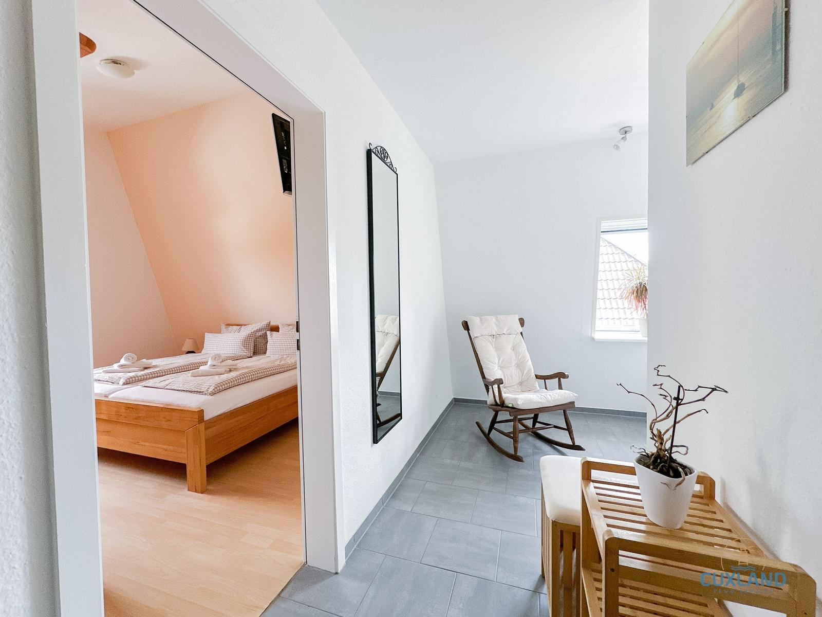 Schlafzimmer mit Dachschrägen und Holzbett. Flur mit Schaukelstuhl und Spiegel.