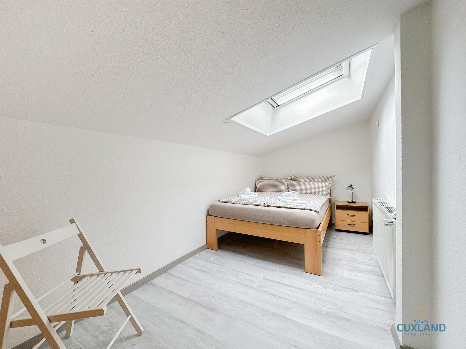 Schlafzimmer mit Dachschrägen, Bett, Nachttisch und Sitzgelegenheit.