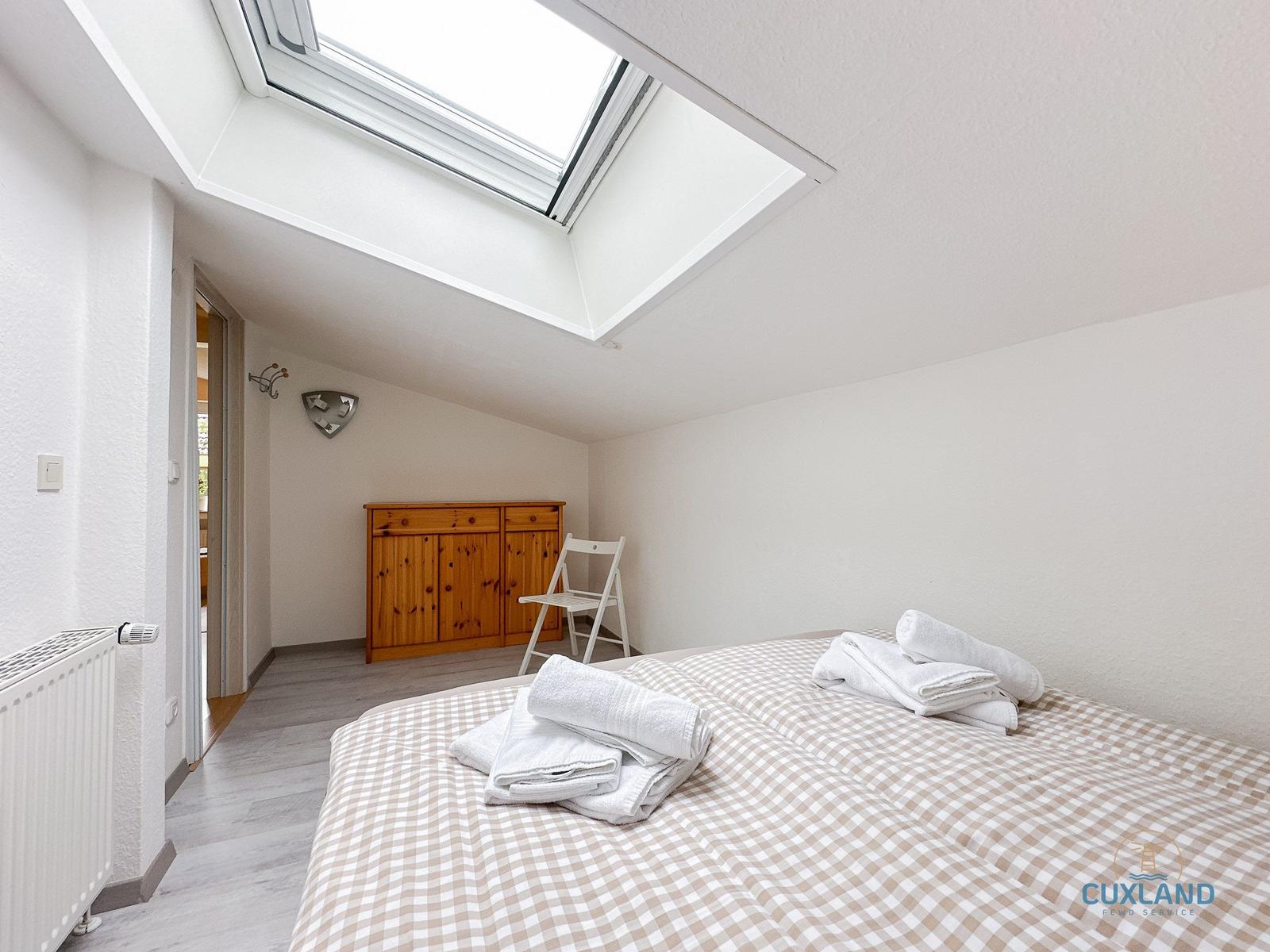 Schlafzimmer mit Dachfenster, Bett und Holzschrank.