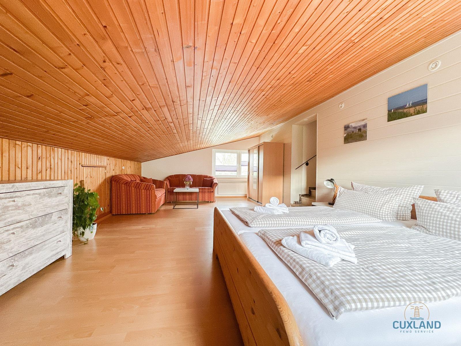 Schlafzimmer mit Doppelbett, Wohnbereich und Holzdecke.