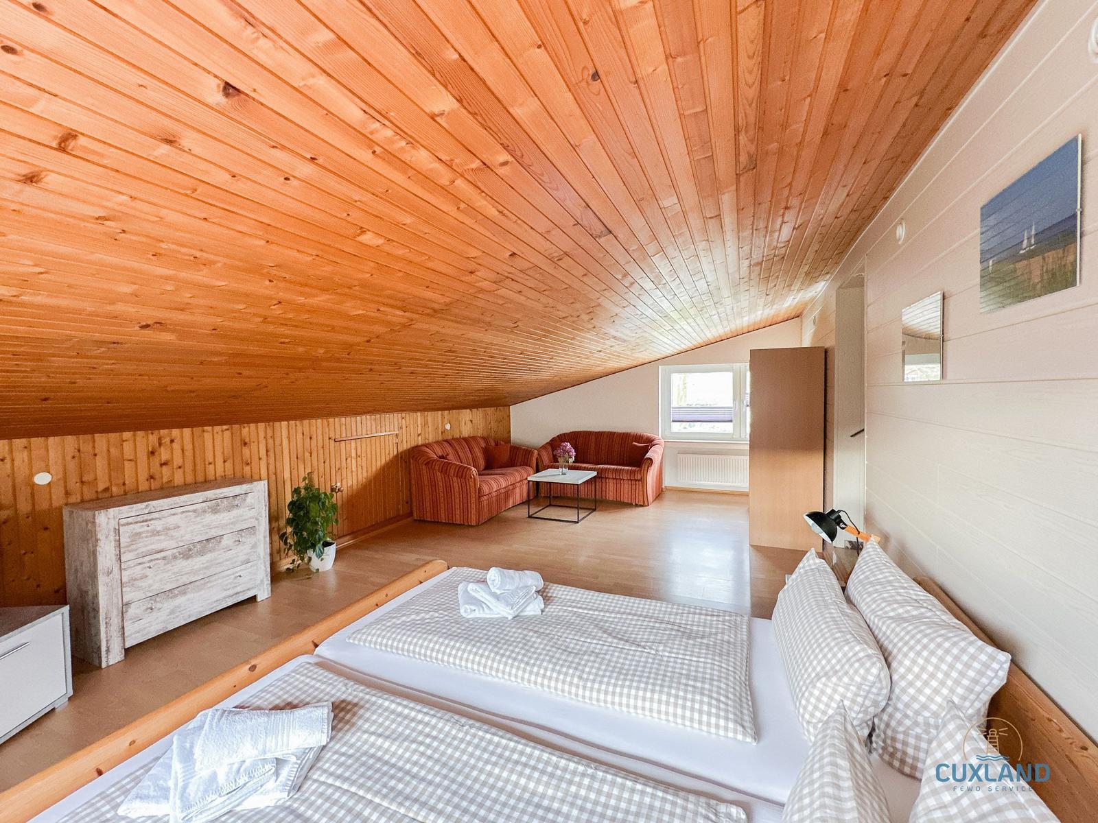 Schlafzimmer mit Doppelbett, Couch und Holzdecke.
