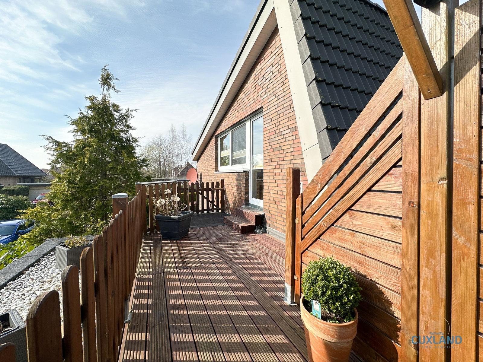 Holzterrasse mit Pflanzen und Blick auf Hauswand.