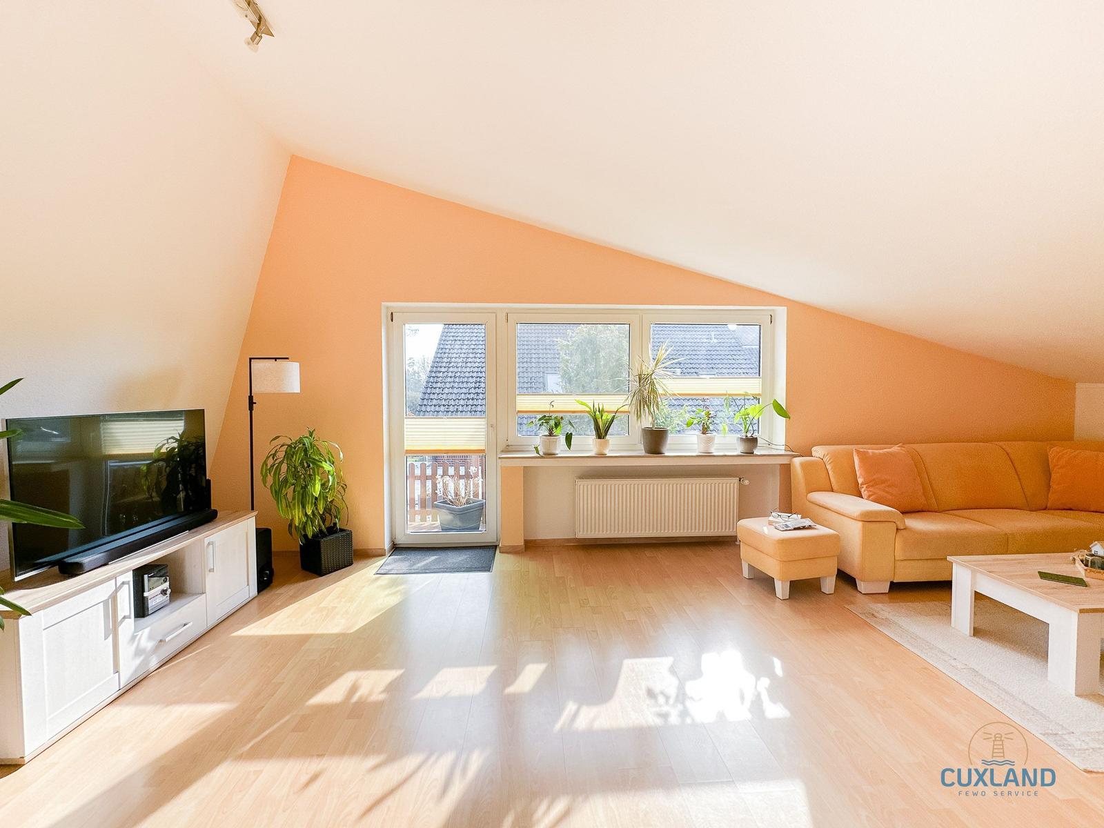 Wohnzimmer mit Sofa, Fernseher und Balkonzugang.