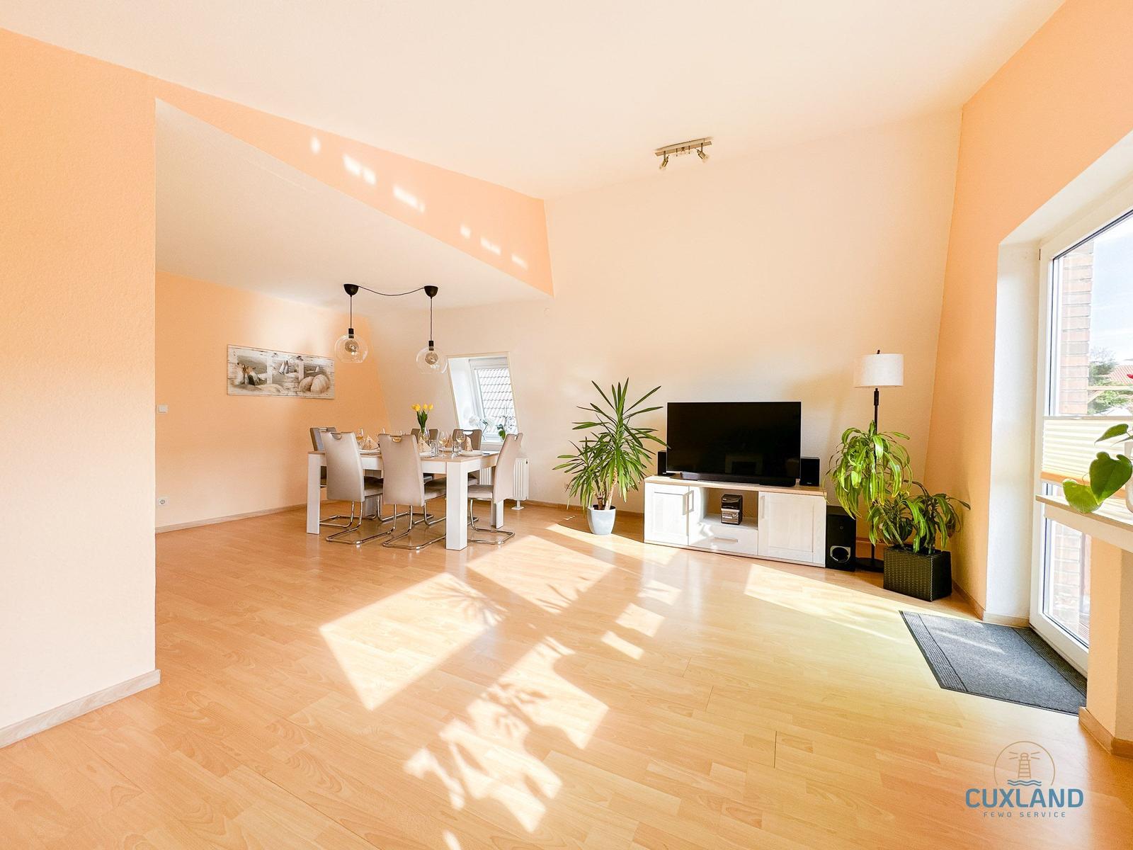 Wohn- und Essbereich mit Holzboden, TV, Pflanzen und Tisch mit Stühlen.