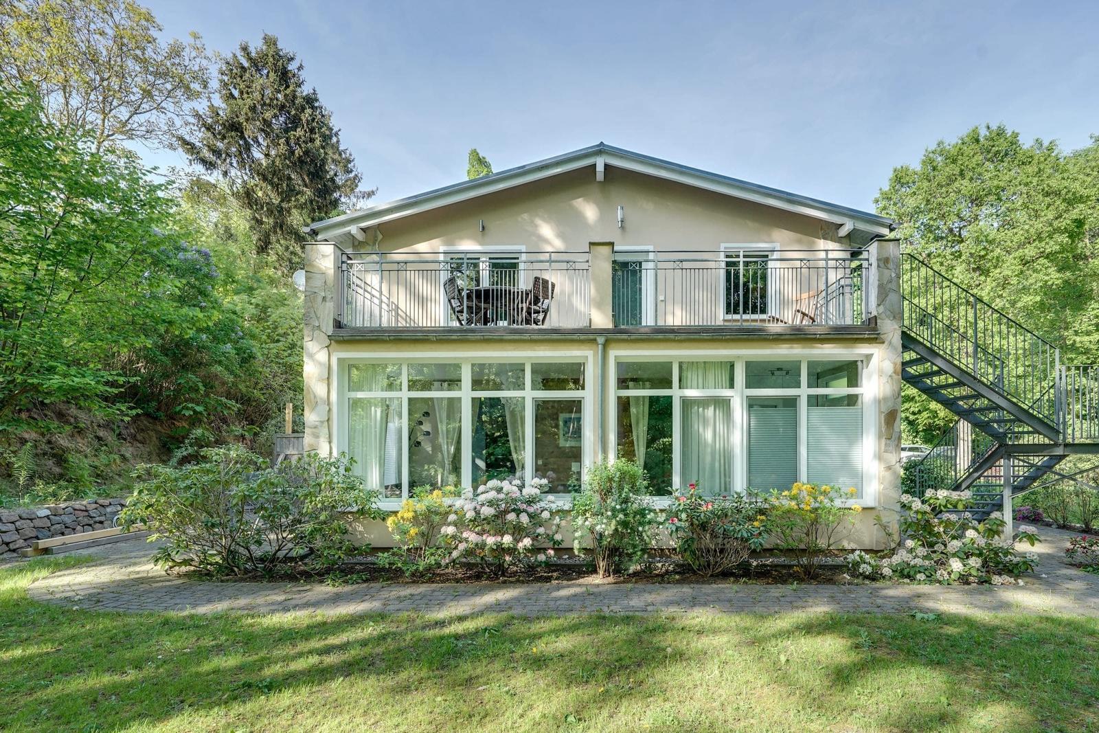 Zweistöckiges Haus mit Balkon, Garten und Blumenbeeten.