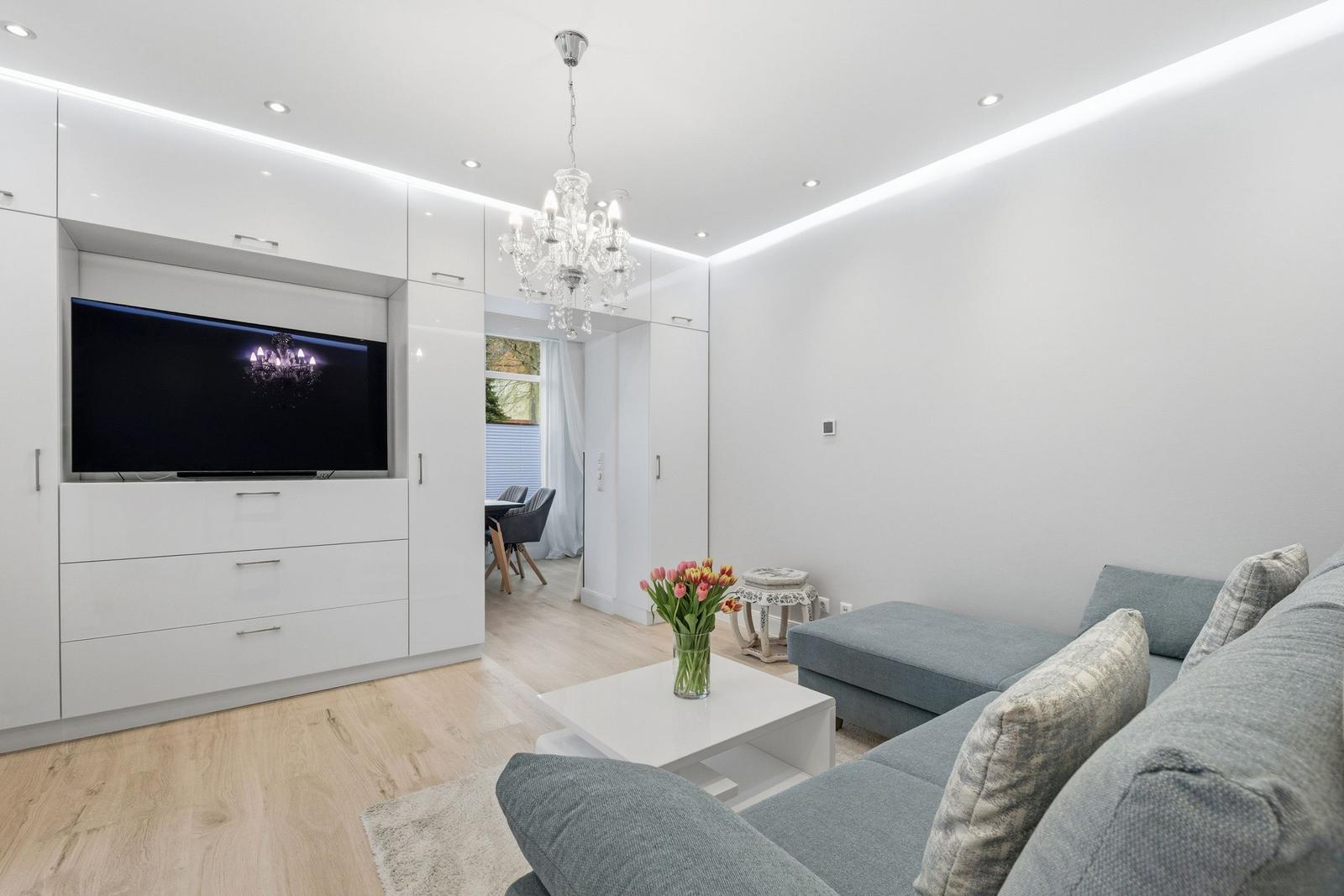 Wohnzimmer mit grauem Sofa, weißem Couchtisch und integriertem Fernseher.